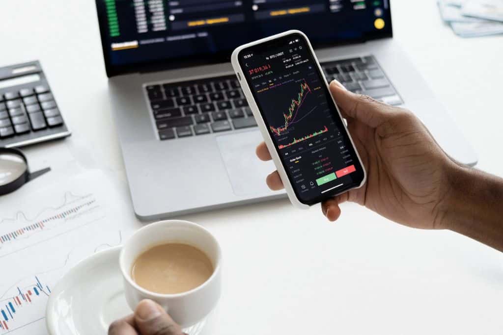 Person looking at the stock market on their phone and laptop screens - TradeZella
